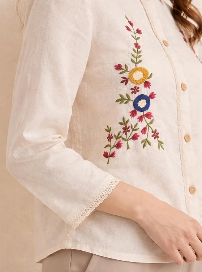 Woman wearing a cream embroidered button-down top with floral detailing and long sleeves, styled with beige pants.