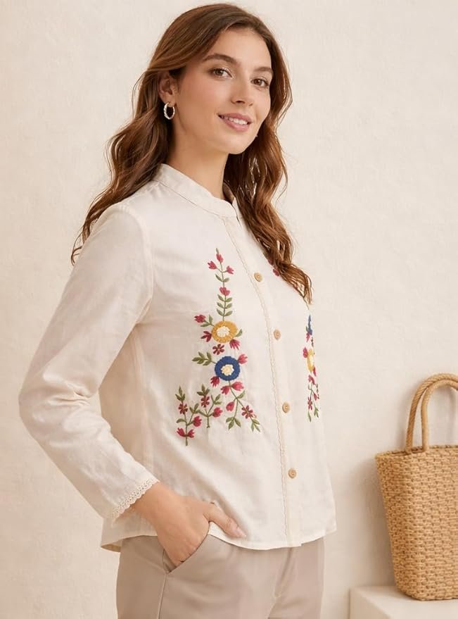 Woman wearing a cream embroidered button-down top with floral detailing and long sleeves, styled with beige pants.