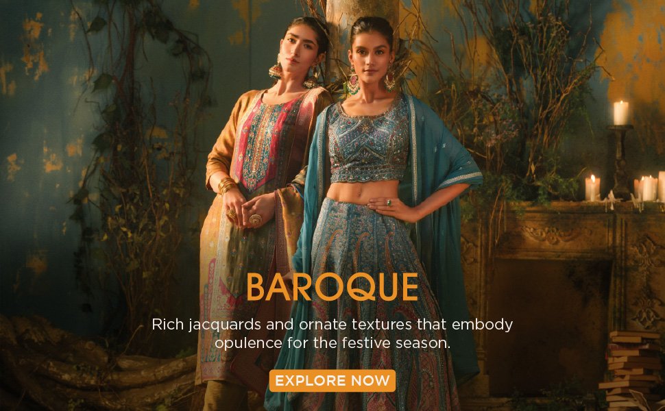 Two women wearing luxurious embroidered ethnic outfits in a festive setting with candles and vintage décor.