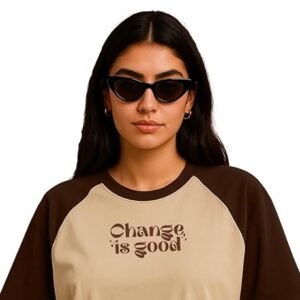 Woman wearing a beige and brown graphic oversized t-shirt with denim skirt and sunglasses against a brown background.