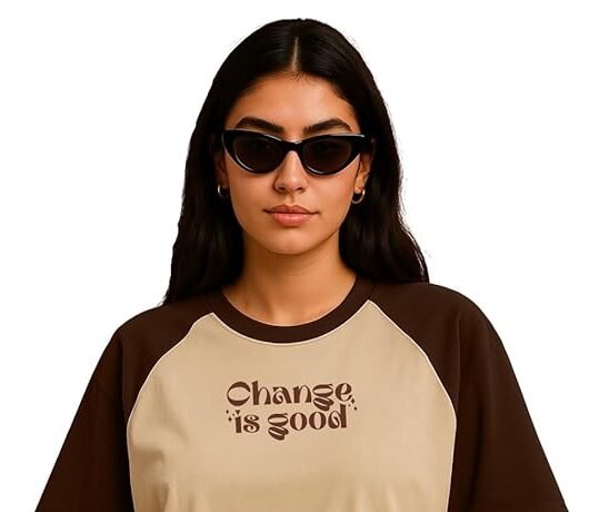 Woman wearing a beige and brown graphic oversized t-shirt with denim skirt and sunglasses against a brown background.
