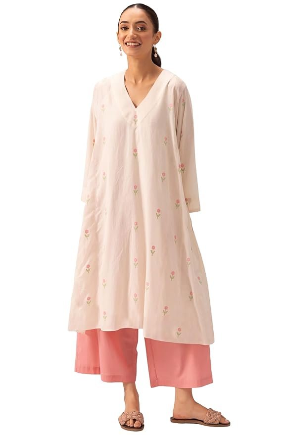 Woman wearing a light pink floral embroidered kurta with pink palazzo pants and flat sandals against a plain background.