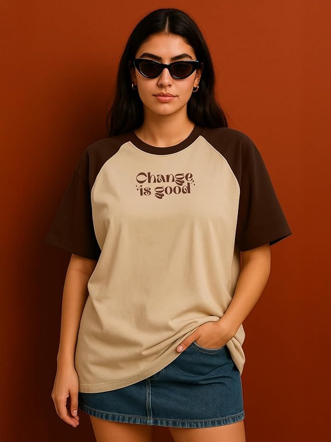 Woman wearing a beige and brown graphic oversized t-shirt with denim skirt and sunglasses against a brown background.