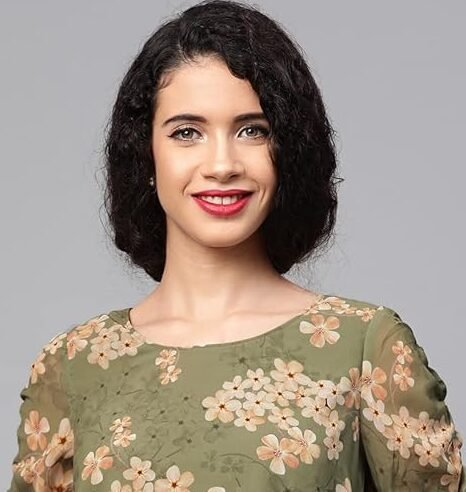 Woman wearing a sage green floral blouse with a cream midi skirt, beige heels, and a matching handbag against a grey background