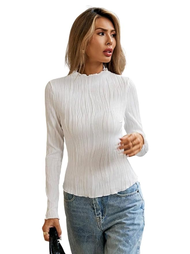 Woman wearing a white textured high-neck top with long sleeves and blue jeans, posing against a plain background.