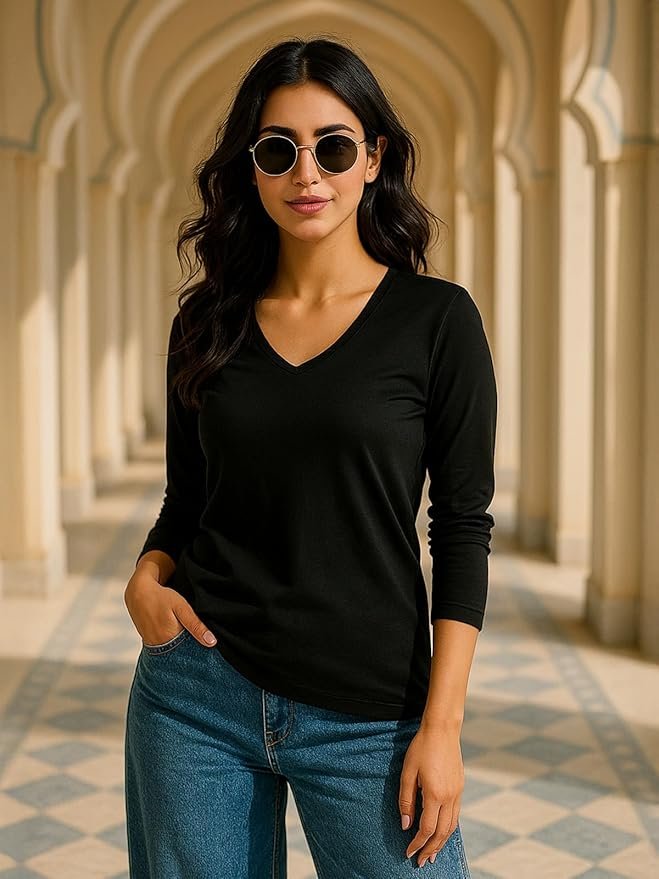 Woman wearing a black V-neck long-sleeve top with blue jeans and sunglasses, posing against a beige background.