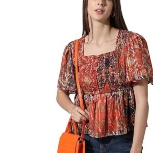 Woman wearing a red printed puff sleeve peplum top paired with distressed blue jeans and heels against a plain background.