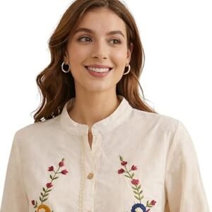 Woman wearing a cream embroidered button-down top with floral detailing and long sleeves, styled with beige pants.