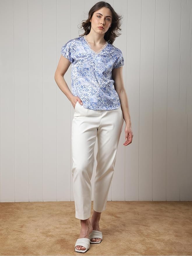 Woman wearing a blue floral print V-neck top with short puff sleeves, posing against a white background.