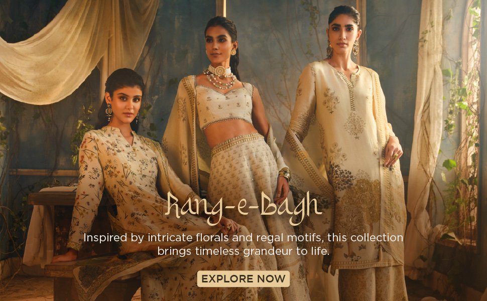 Two women wearing luxurious embroidered ethnic outfits in a festive setting with candles and vintage décor.