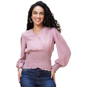 Woman wearing a pink textured smocked blouse with long sleeves and blue jeans on a grey background